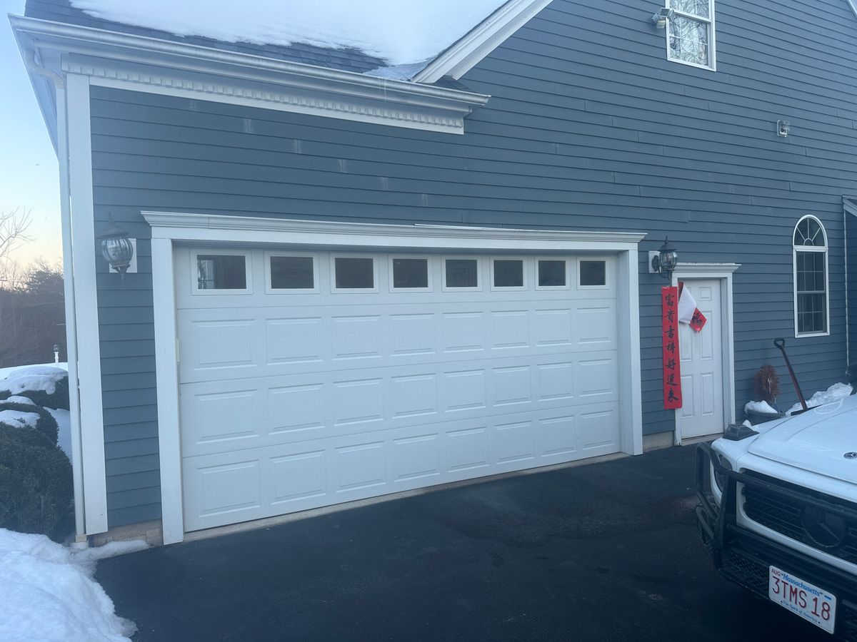 White garage door with decorative windows on blue colonial home in winter