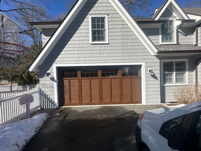 Custom wood craftsman garage door with transom windows on gray shingle home in winter